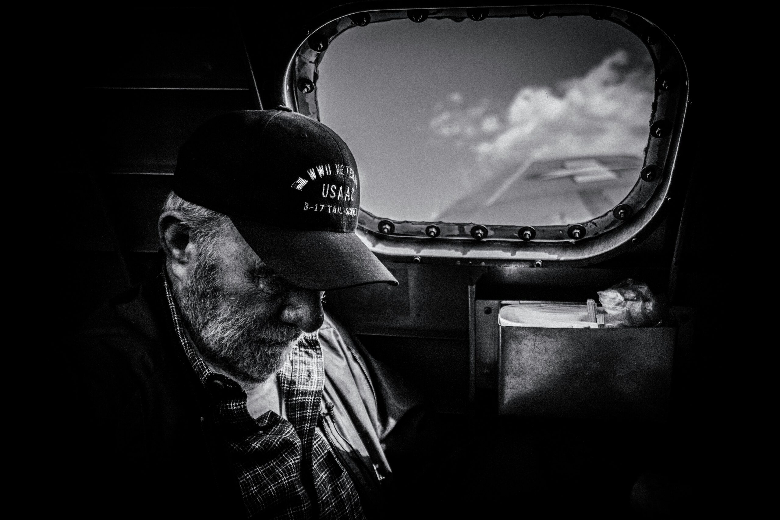 Black and white silhouette of a veteran wearing a cap with his head bowed against a bright window.